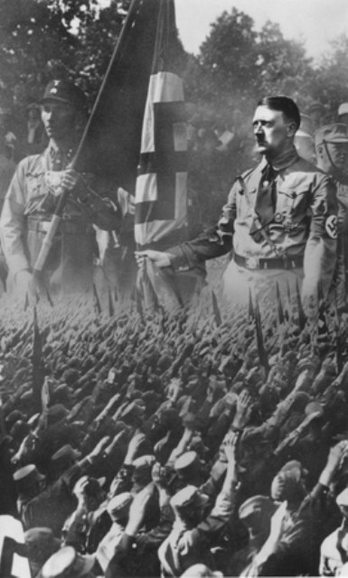 Picture postcard showing a crowd of saluting Germans superimposed on an enlarged image of Hitler and a Nazi stormtrooper. [LCID: 14951]